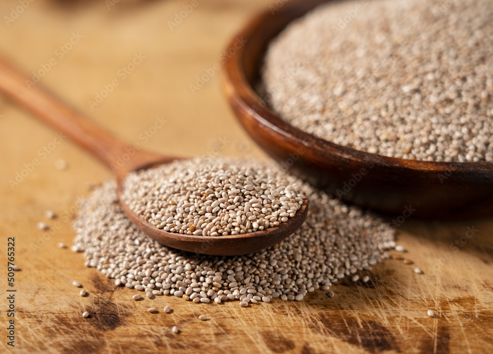 White chia seeds and wooden spoon in a wooden dish placed on a wooden background.