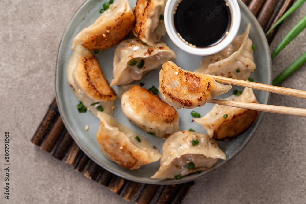 Pan-fried gyoza dumpling jiaozi in a plate with soy sauce on gray table background.