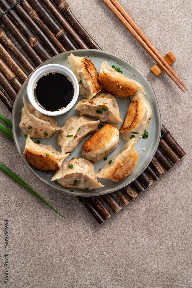 Pan-fried gyoza dumpling jiaozi in a plate with soy sauce on gray table background.