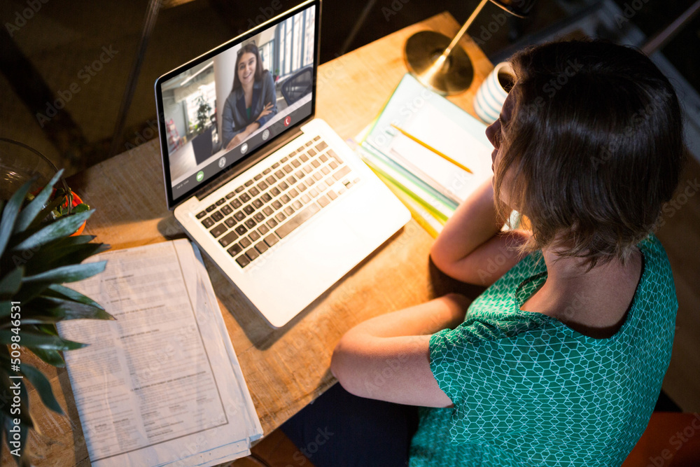 Smiling caucasian businesswoman on video call with caucasian female colleague sitting at desk