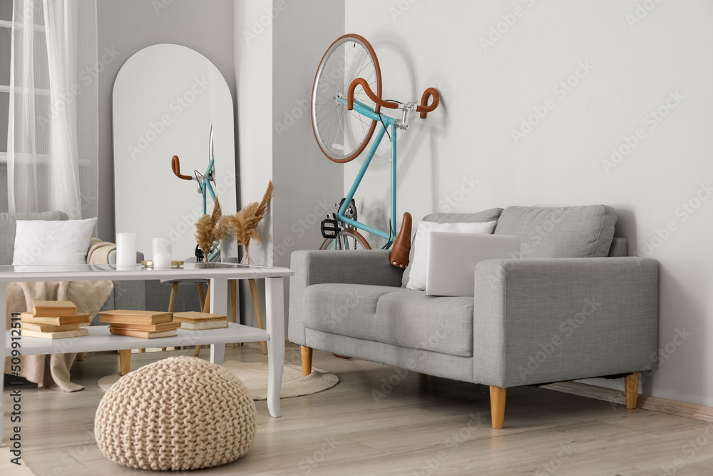 Interior of light living room with bicycle, grey sofas and table