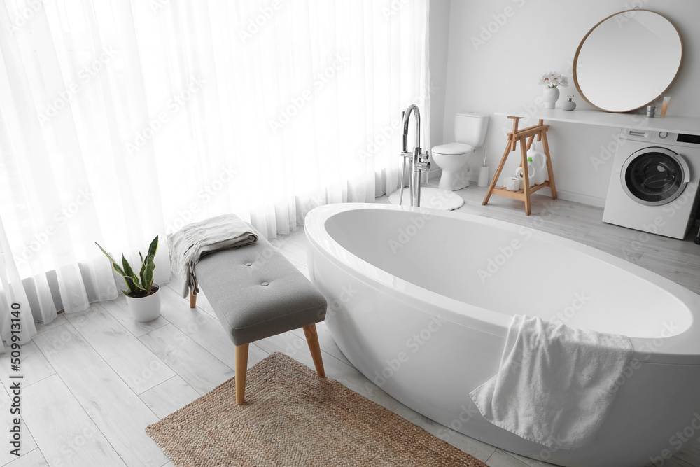 Interior of light room with soft bench, bathtub and washing machine