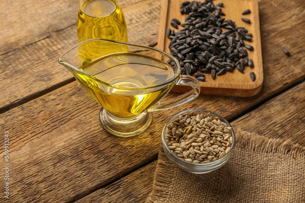 Board, bowl with sunflower seeds and oil on wooden background