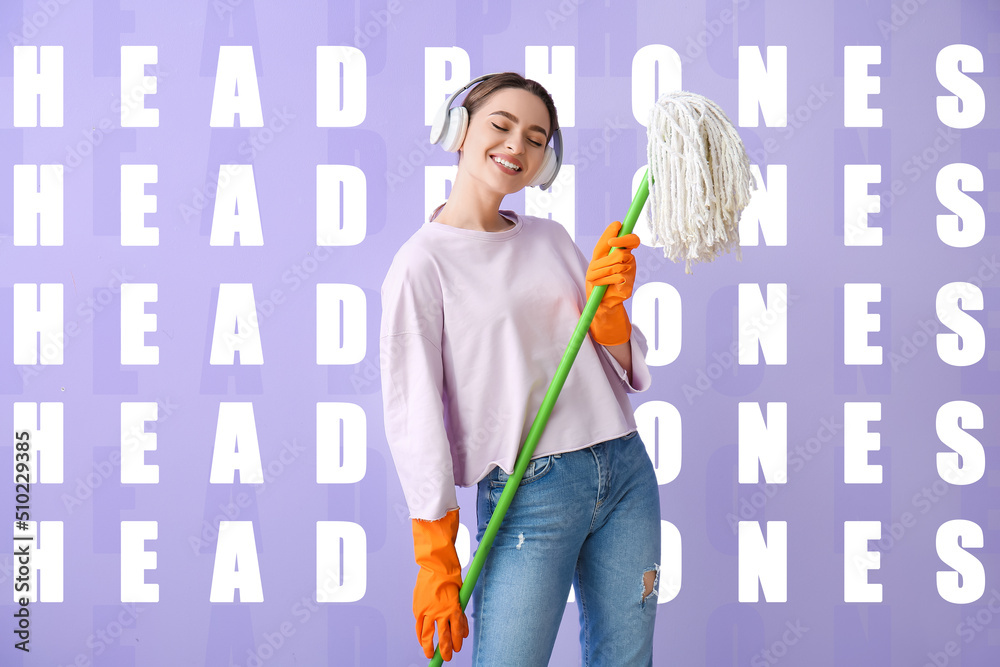 Young woman with floor mop listening to music on lilac background with words HEADPHONES