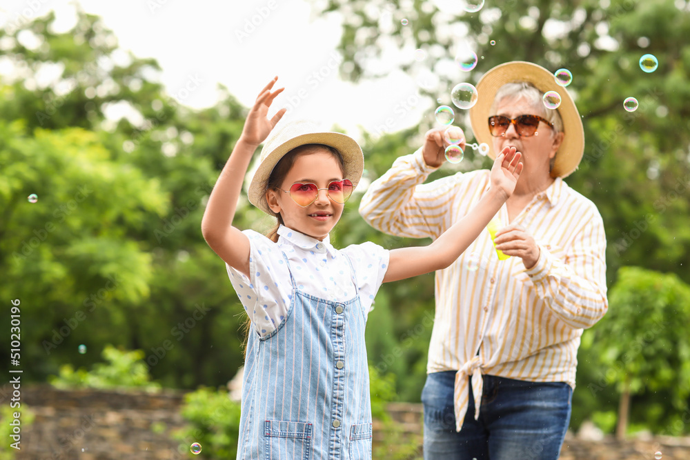 Little girl and her grandma blowing soap bubbles in park