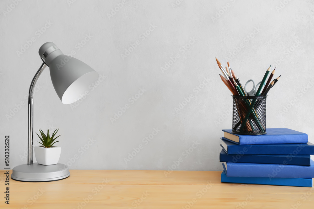 Modern lamp and different stationery on table near light wall