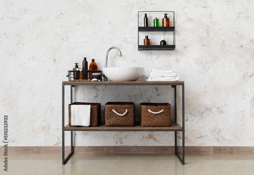 Table with sink, baskets and bath accessories near light wall