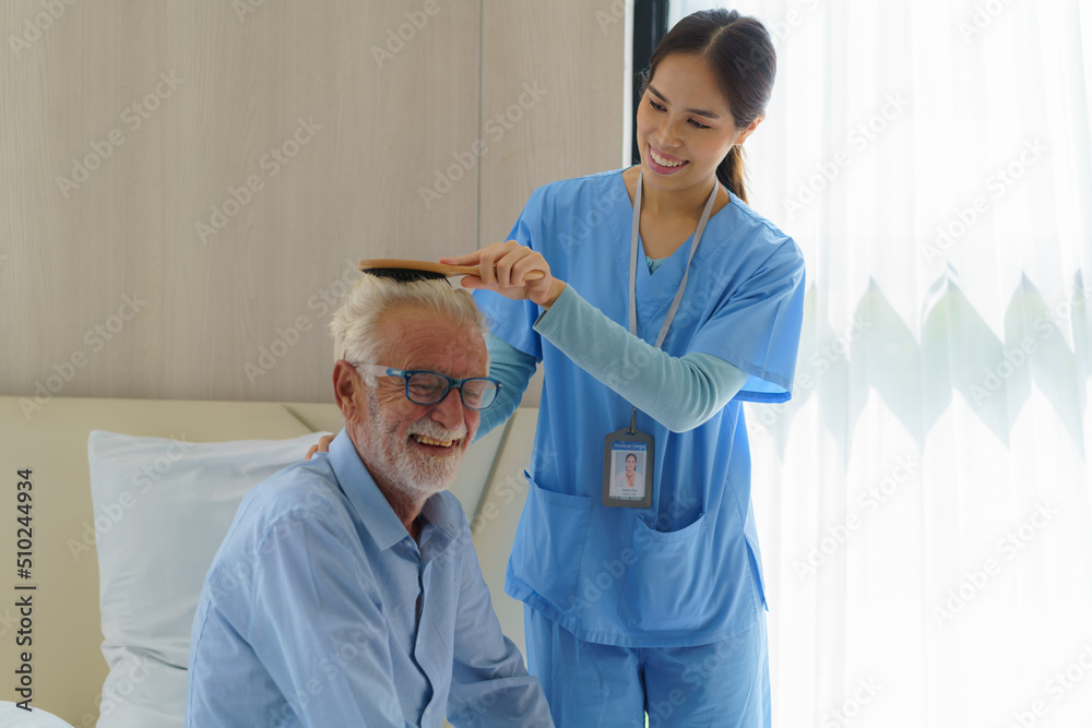 Young Asian woman nurse helping brushing hair to disabled elderly man in bed at retirement home. Mil