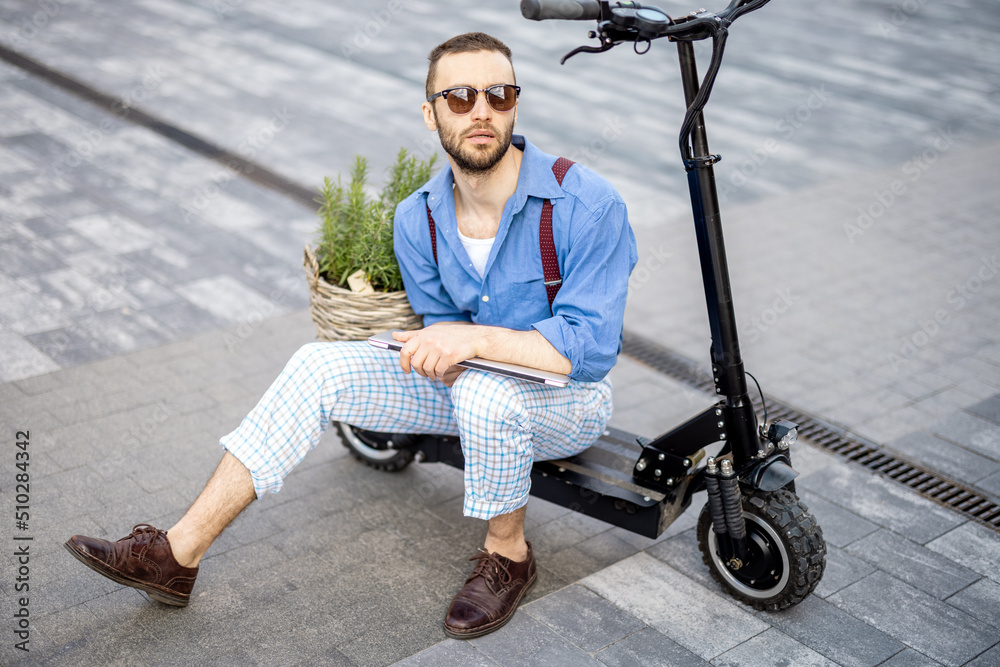 Portrait of stylish weird man sit with laptop on electric scooter outdoors