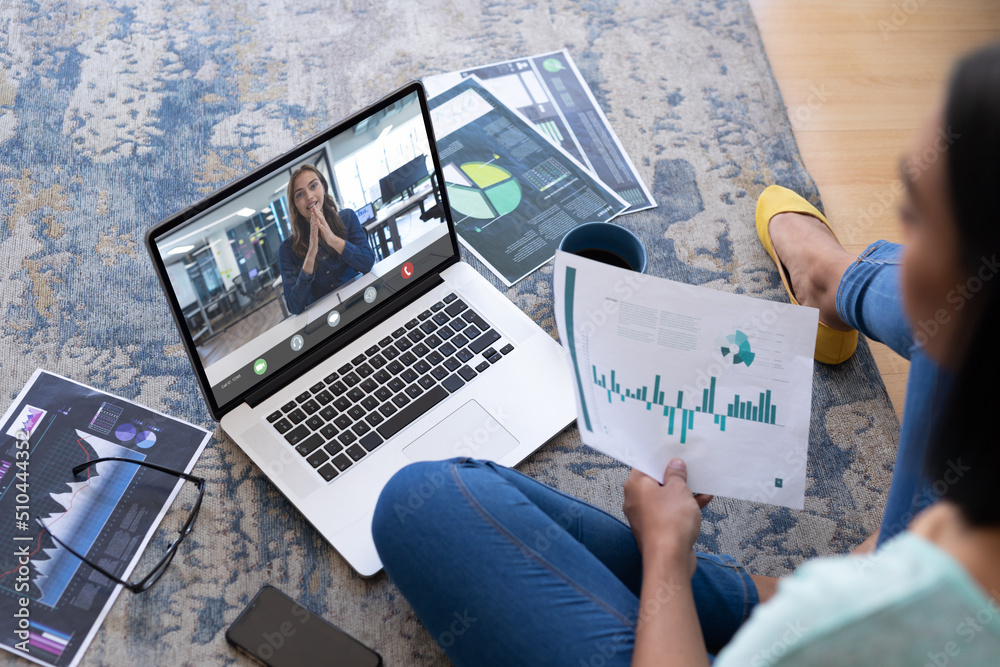 Caucasian businesswoman holding graph discussing with colleague over laptop on carpet