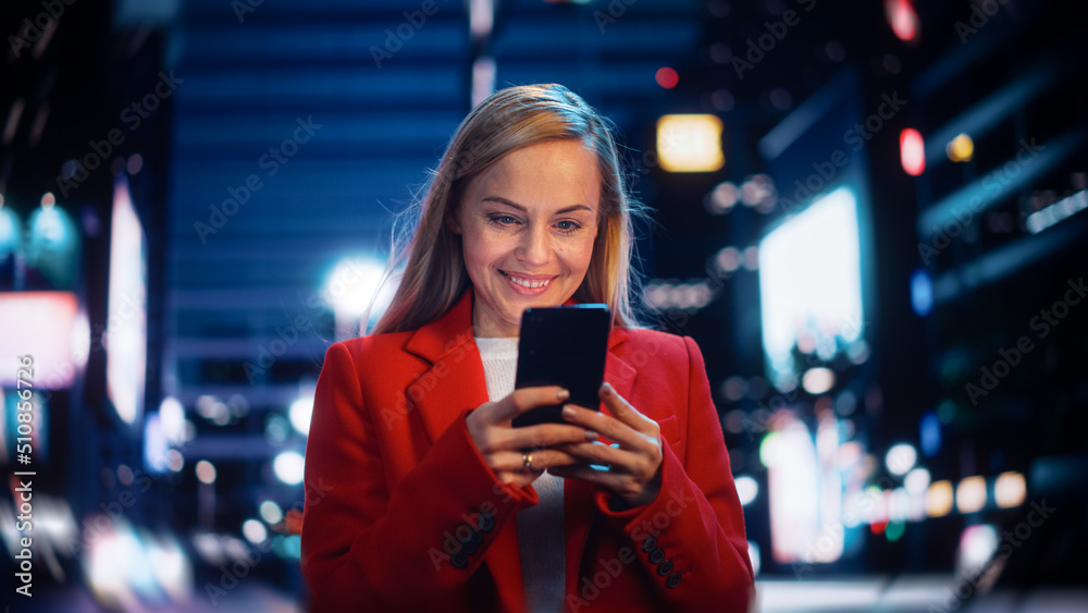 Beautiful Woman Standing, Using Smartphone on City Street with Neon Bokeh Lights Shining at Night. C