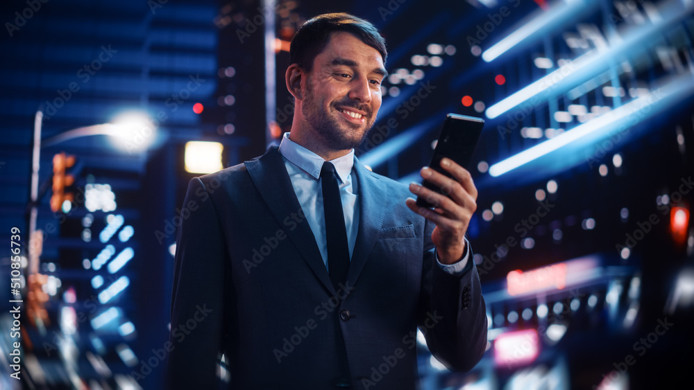 Portrait of a Handsome Man in Stylish Suit Standing in a Modern City Street with Neon Lights at Nigh