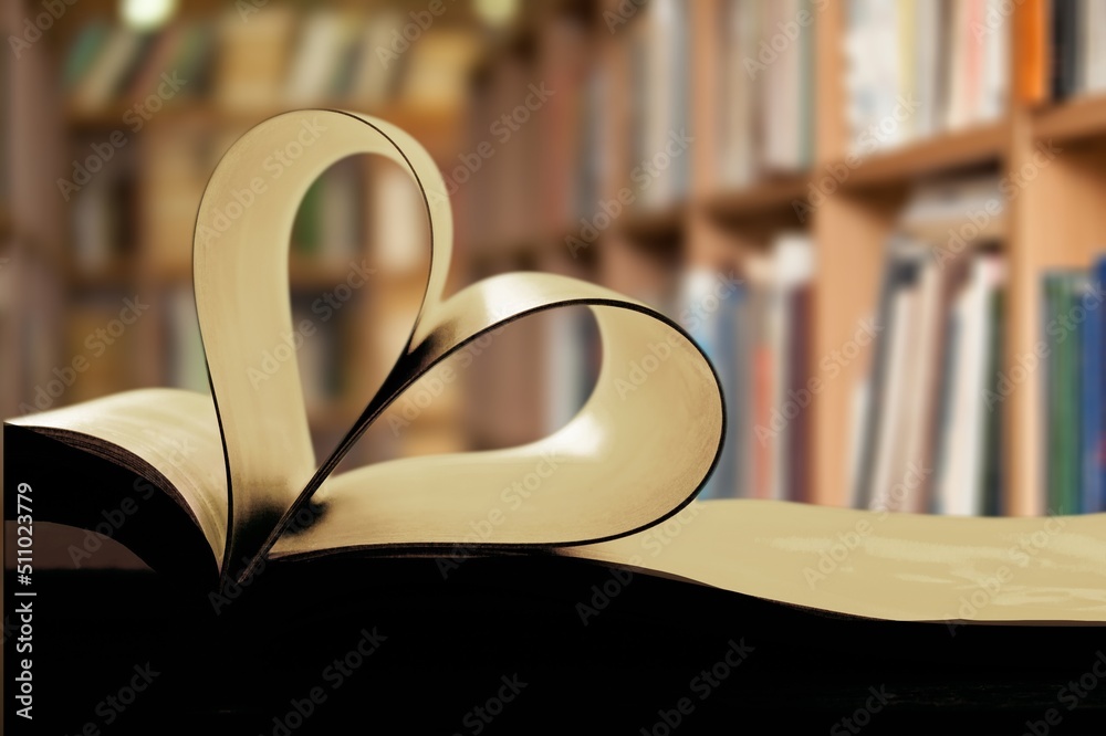 An open book forming a heart with two pages in the center, in the library. In the background are she