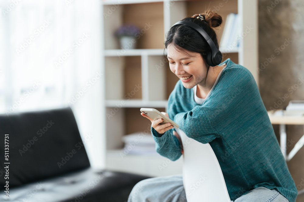 戴着现代无线耳机的宁静女孩坐在舒适的沙发上放松，听音乐，亚洲人