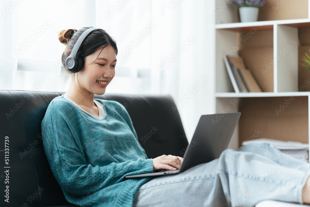 Beautiful smiling young woman in headphones chatting via laptop computer video call at home