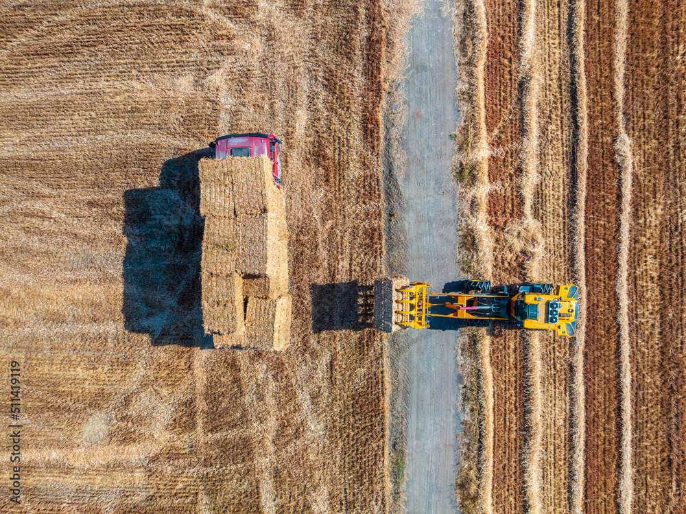 Agricultural tractor loads wheat straw on truck. Aerial view. agricultural machinery. Hay stacks aft