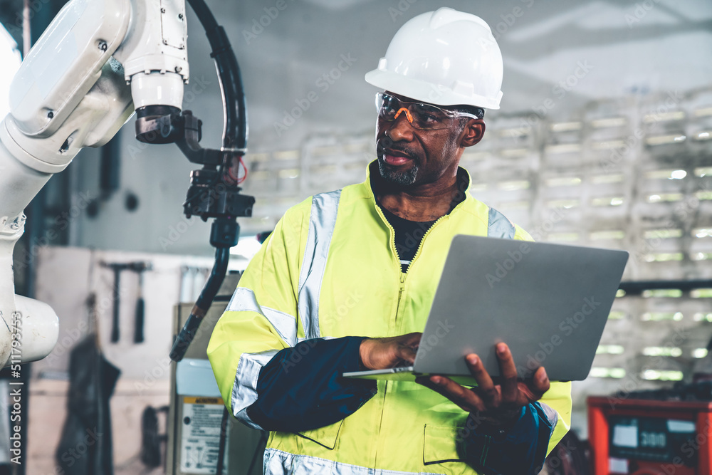 African American factory worker working with adept robotic arm in a workshop . Industry robot progra