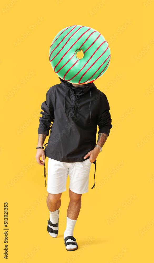 Stylish tattooed man with tasty doughnut instead of his head on yellow background