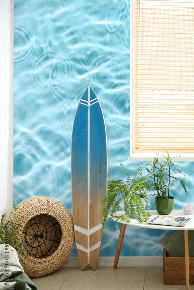 Interior of modern stylish room with surfboard and table near wall with print of clear blue water