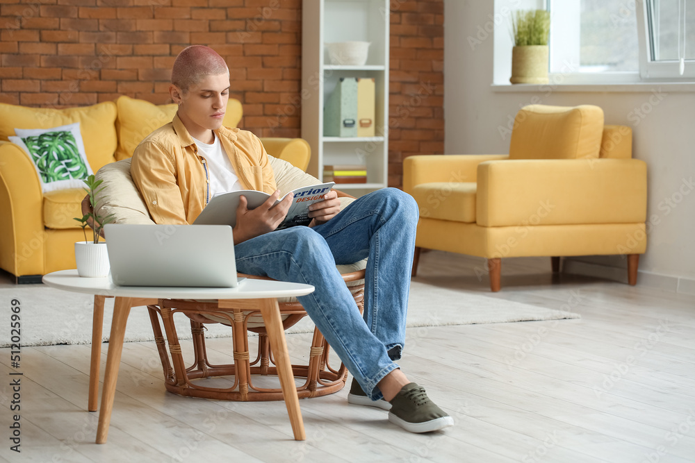 Young guy reading magazine in armchair at home