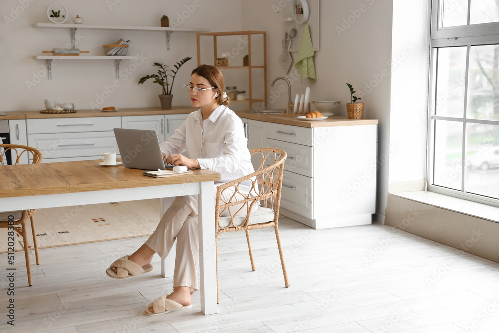 Young female freelancer working on laptop in kitchen