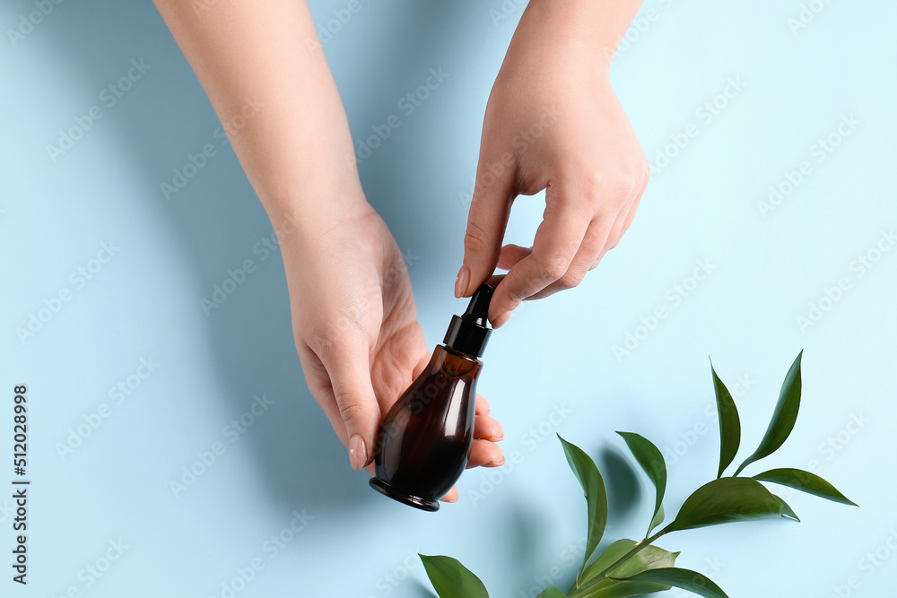 Female hands with bottle of natural serum and plant branch on color background, closeup