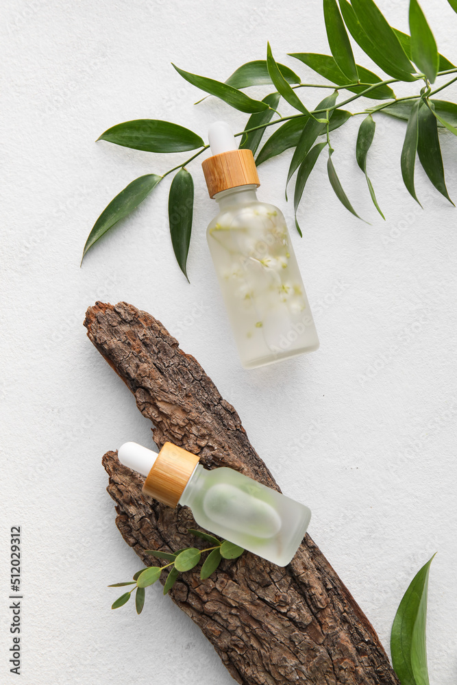 Bottles of natural serum, tree bark and plant leaves on light background