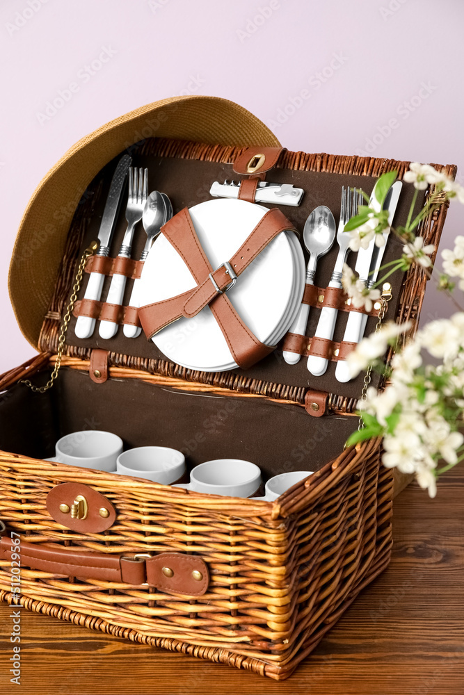 Wicker basket with dishware for picnic on table near light wall, closeup