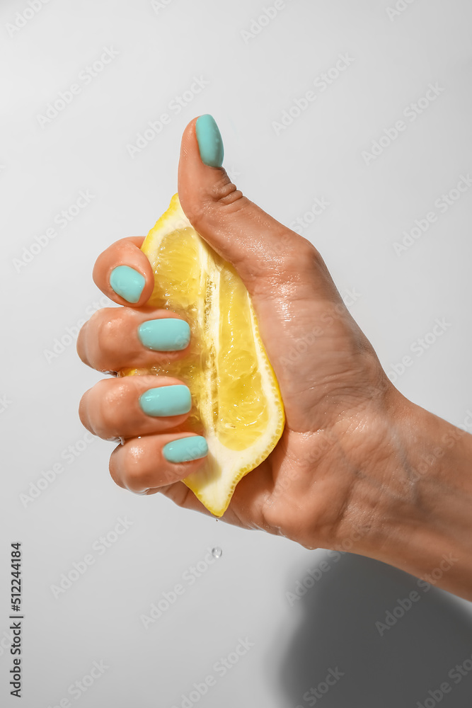 Hand with beautiful mint manicure squeezing lemon on light background