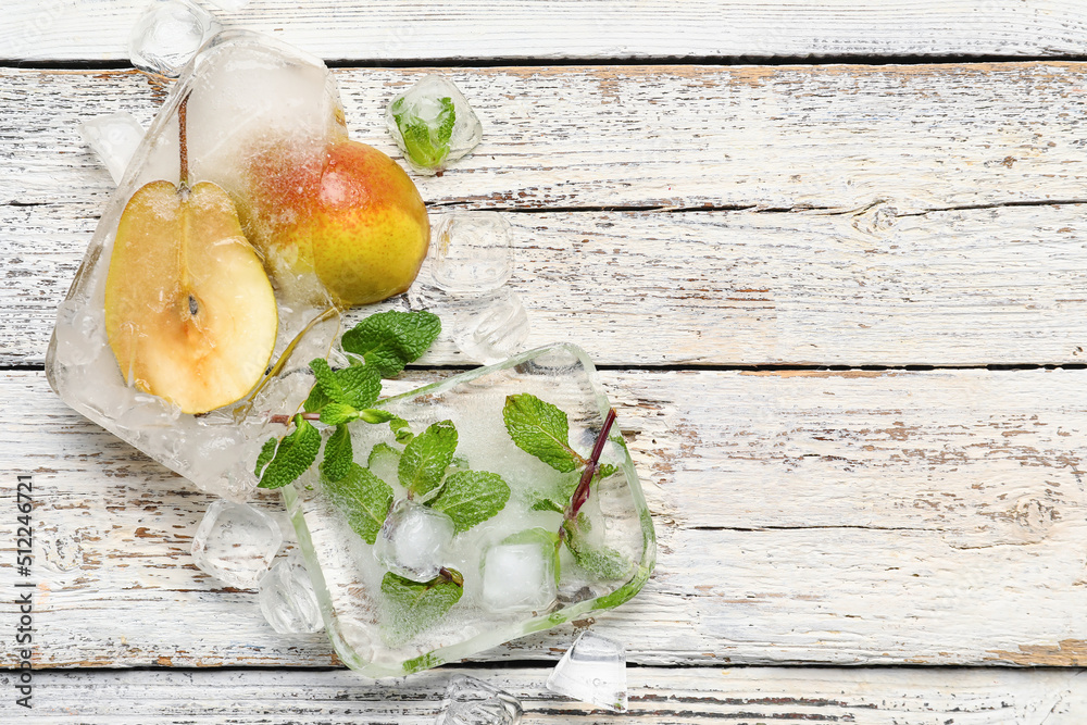 Fresh pear and mint frozen in ice on white wooden background