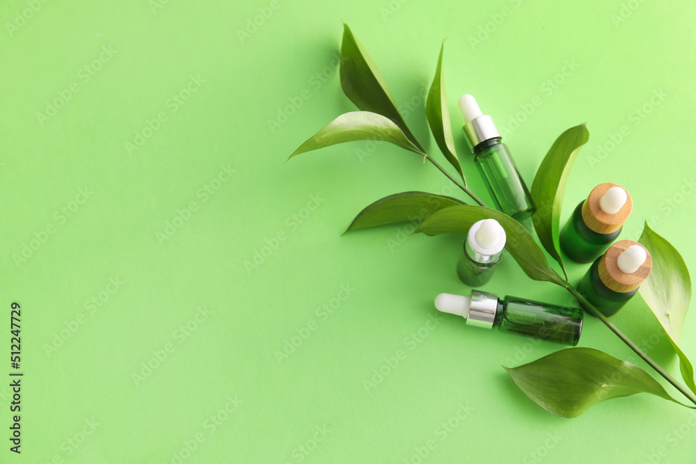 Bottles of natural serum and plant leaves on green background