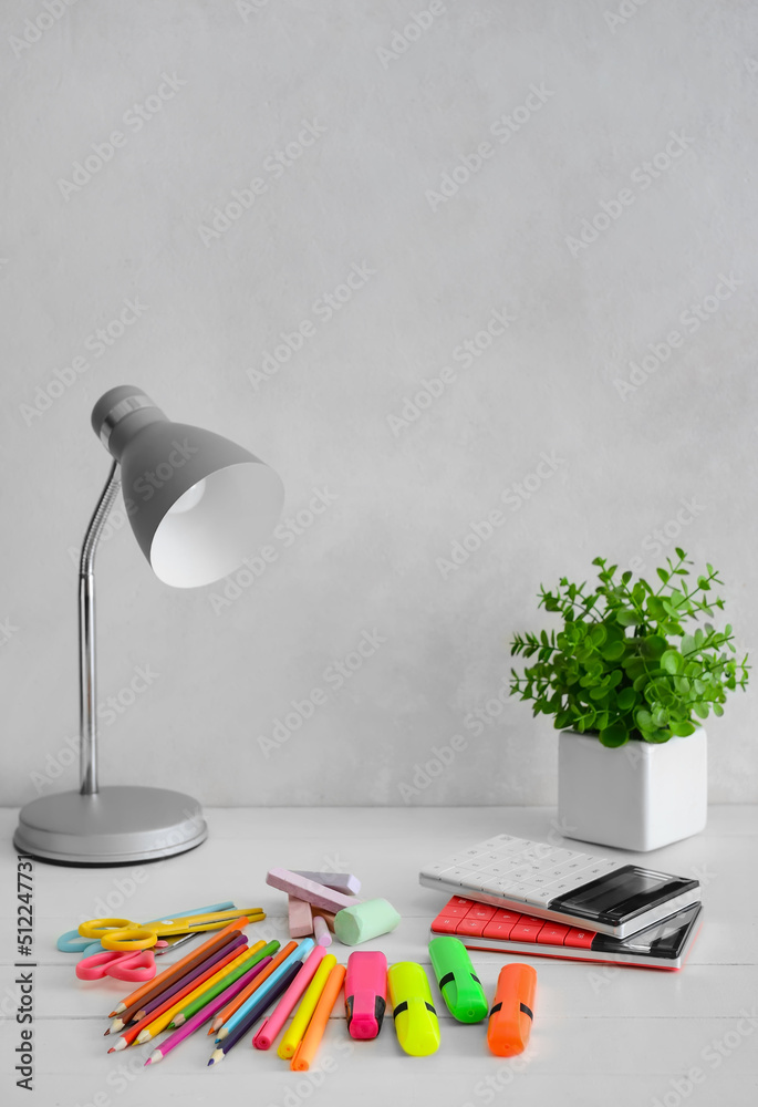 Modern lamp and different stationery on table near light wall