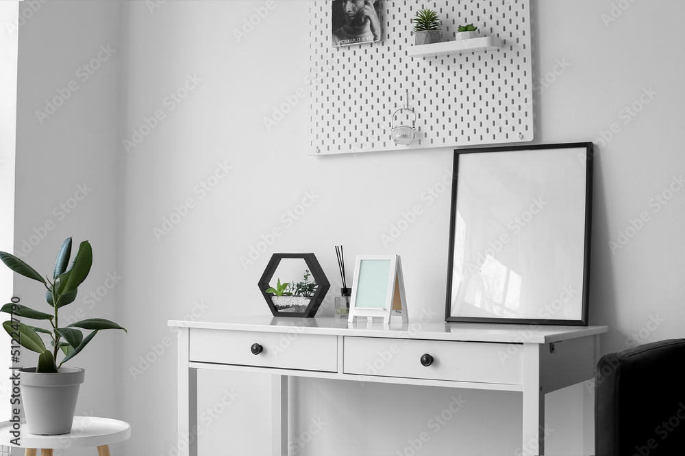 Table with blank frames, reed diffuser and planter near light wall in room