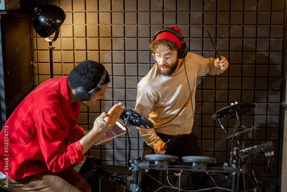 Two stylish men playing electric drums, composing electronic music at small recording studio. Small 