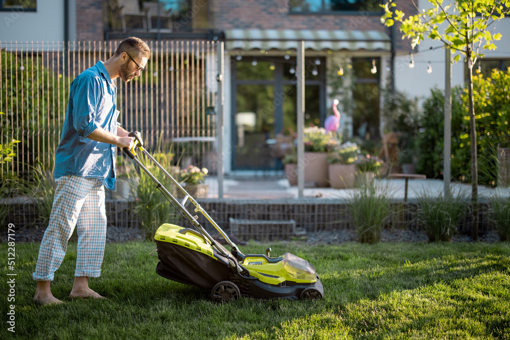 Man mows the lawn with lawn mower at backyard of his house. Husband takes care of garden on summer e