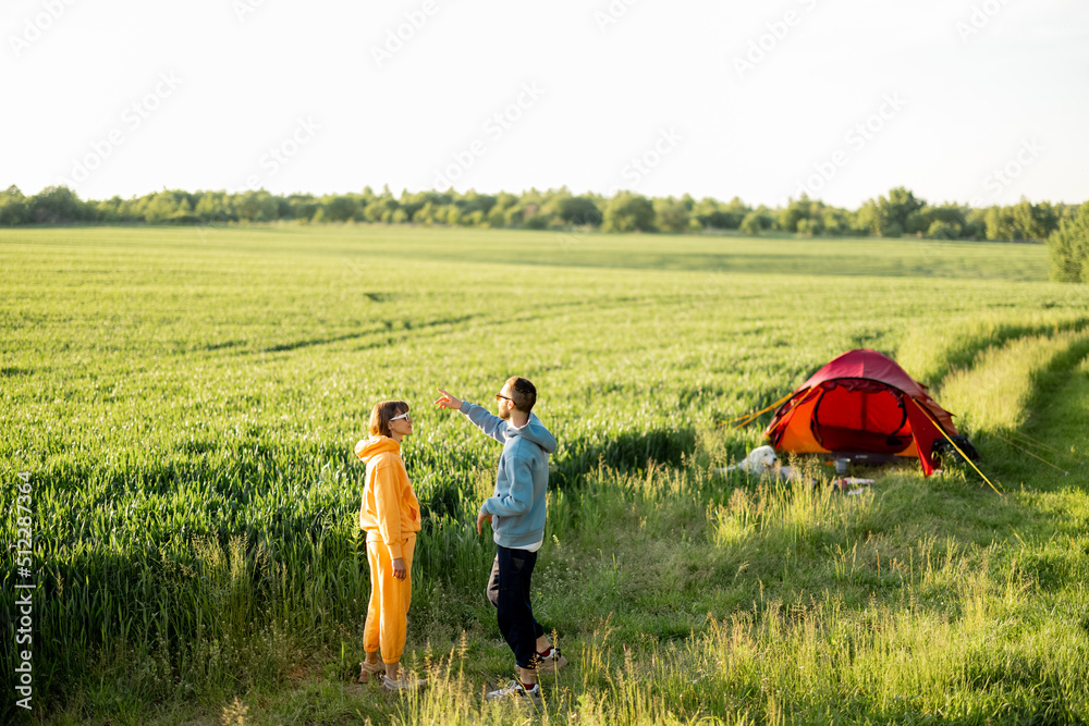 年轻夫妇在夏天带着帐篷在绿地上旅行时，一起散步和聊天，玩得很开心