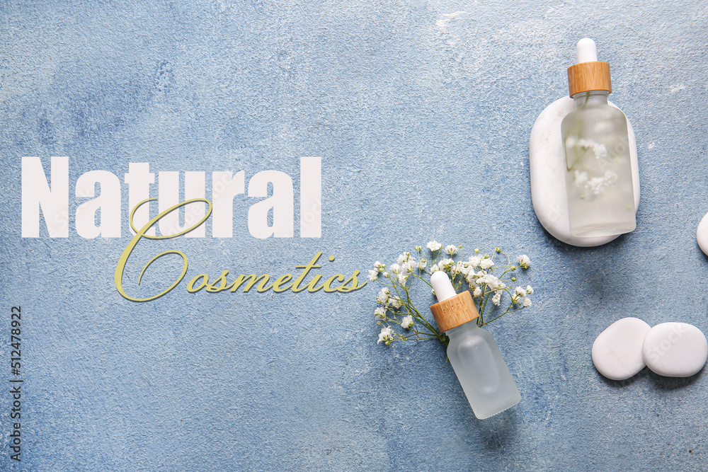 Bottles of essential oils, flowers, spa stones and text NATURAL COSMETICS on light blue background