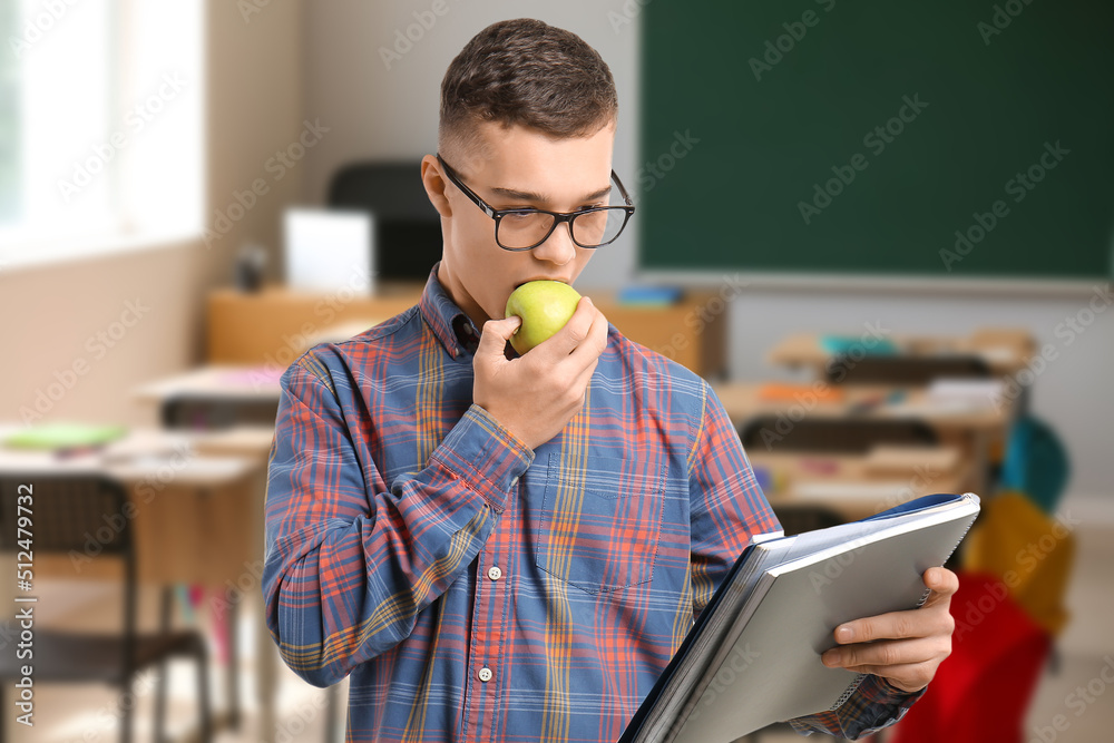 Male student eating apple in classroom