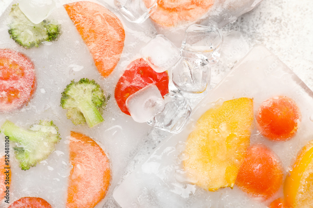 Fresh cut vegetables frozen in ice on light background