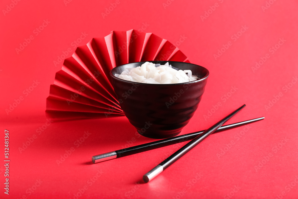 Bowl with tasty noodles and chopsticks on red background