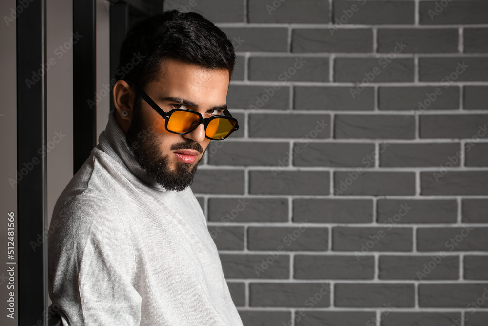 Young bearded man wearing stylish sunglasses near grey brick wall