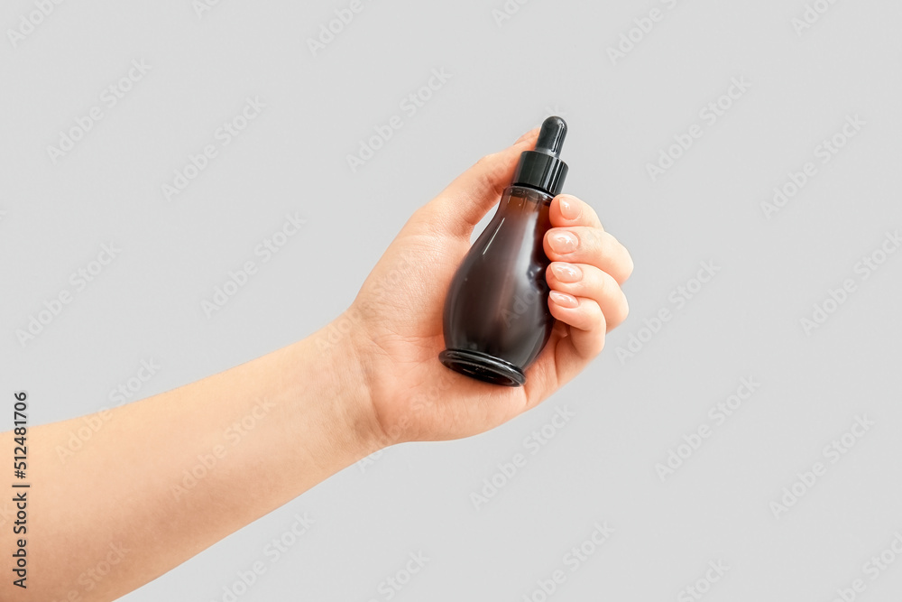 Female hand with bottle of serum on light background, closeup