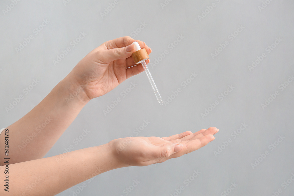 Woman applying serum onto her hand on light background