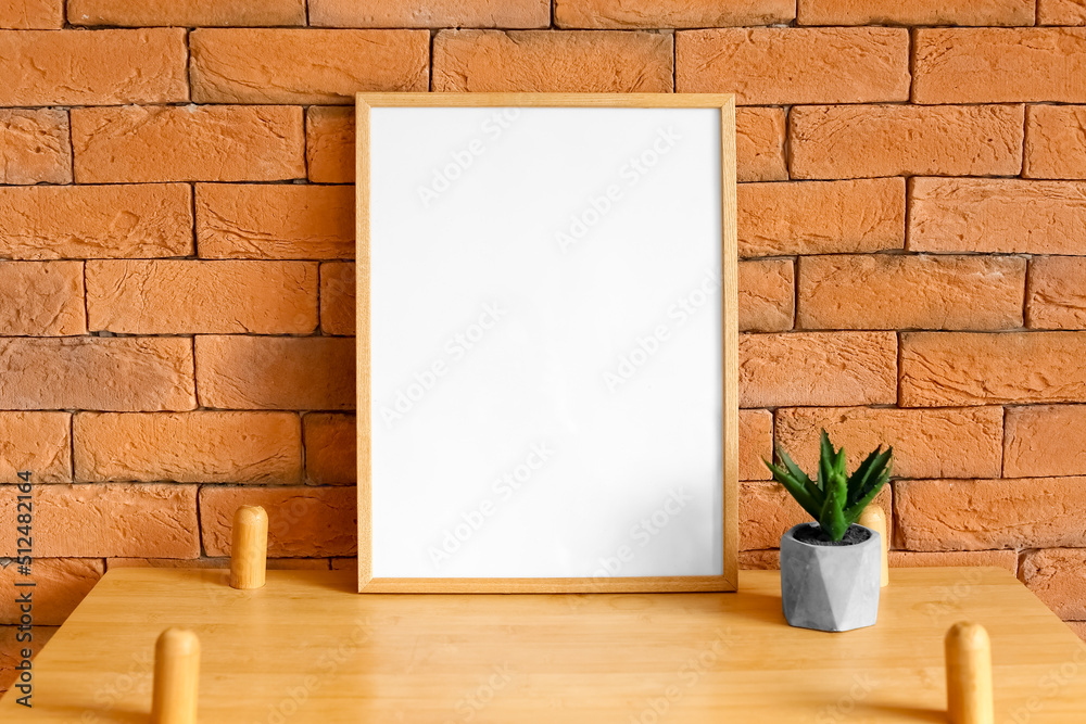 Big blank frame and flowerpot on shelf near brick wall