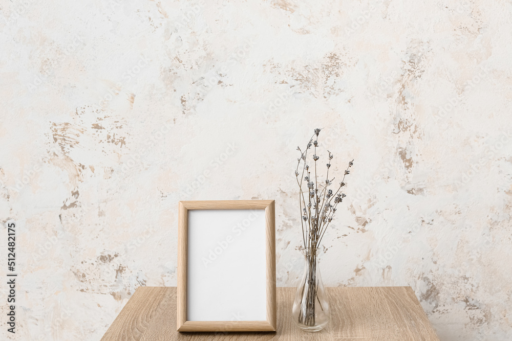 Blank frame and vase with flowers on table near light wall