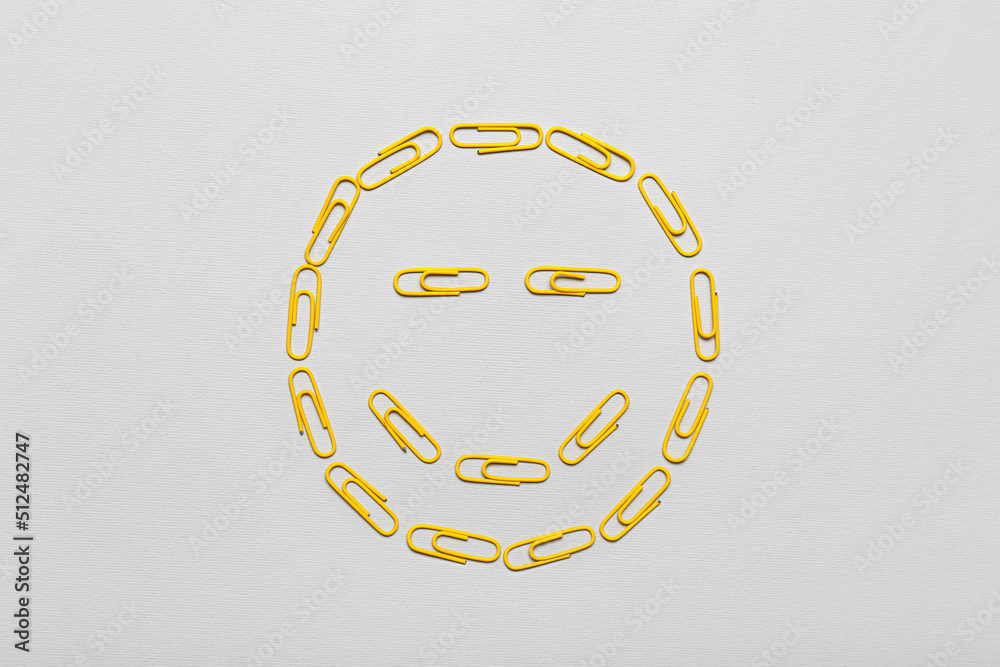 Smile made of yellow paper clips on light background