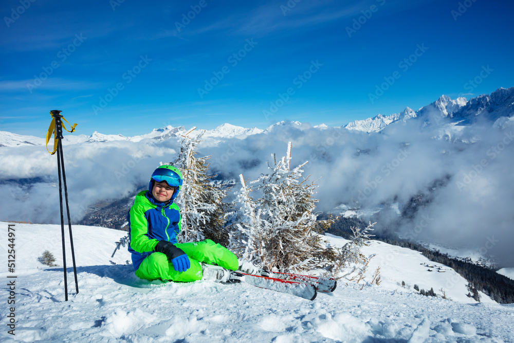 Ski boy sit resting on top of the mountain covered by clouds