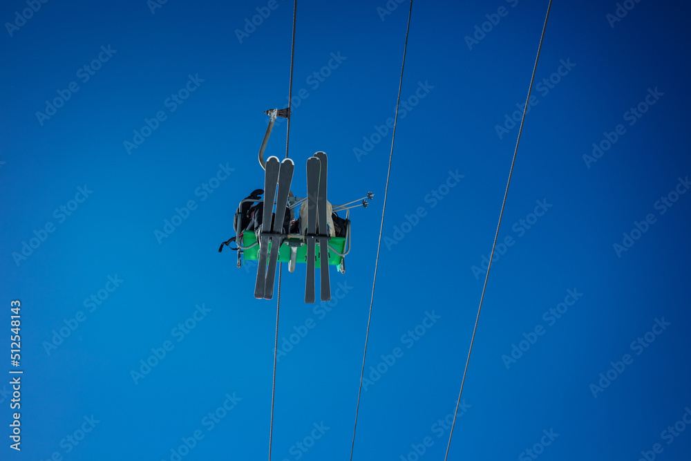 Alpine ski lift seat and bottoms of skis over blue sky