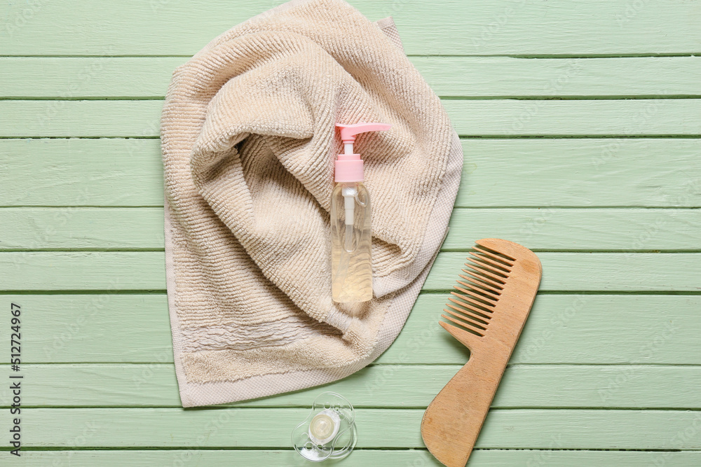 Baby hair comb, pacifier and bath accessories on green wooden background