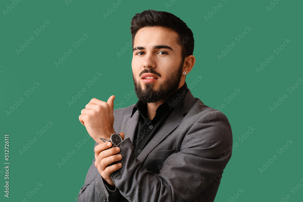 Young bearded man wearing stylish wristwatch on green background